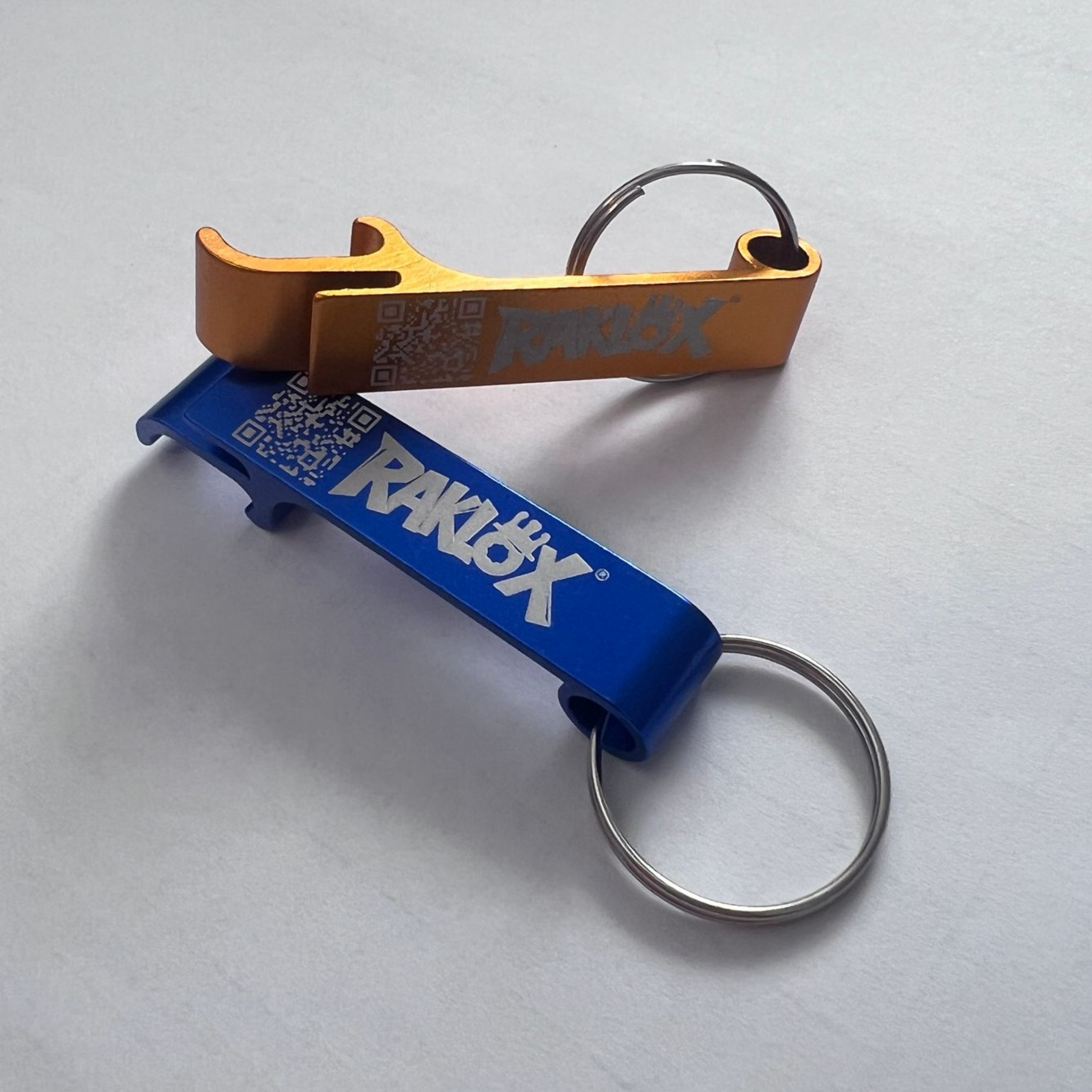 Two bottle openers, one blue and one gold, with 'RAKLOX' branding on a light gray background.