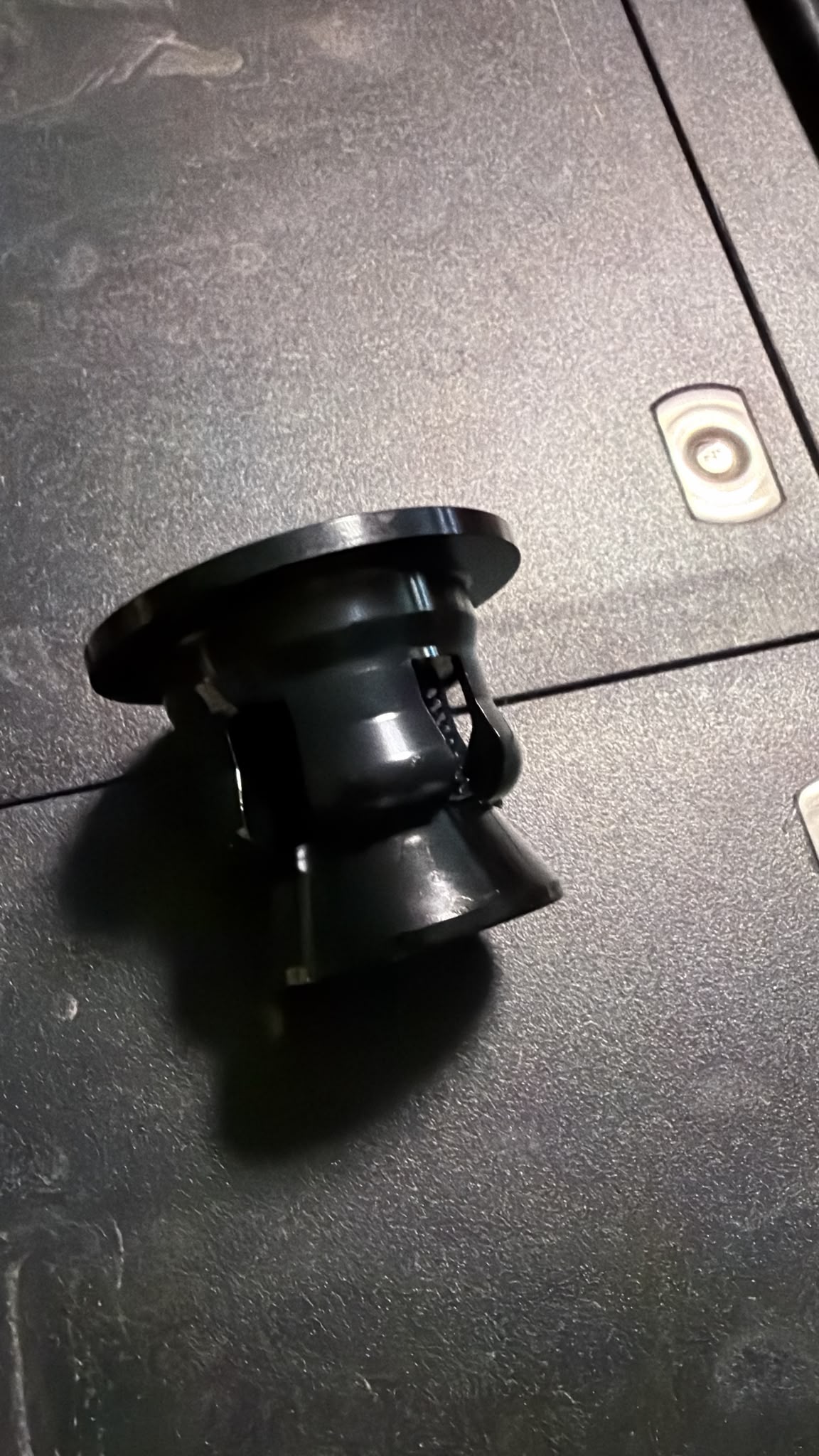 A steel mounting bracket or adapter with a circular base, photographed on a dark textured surface.