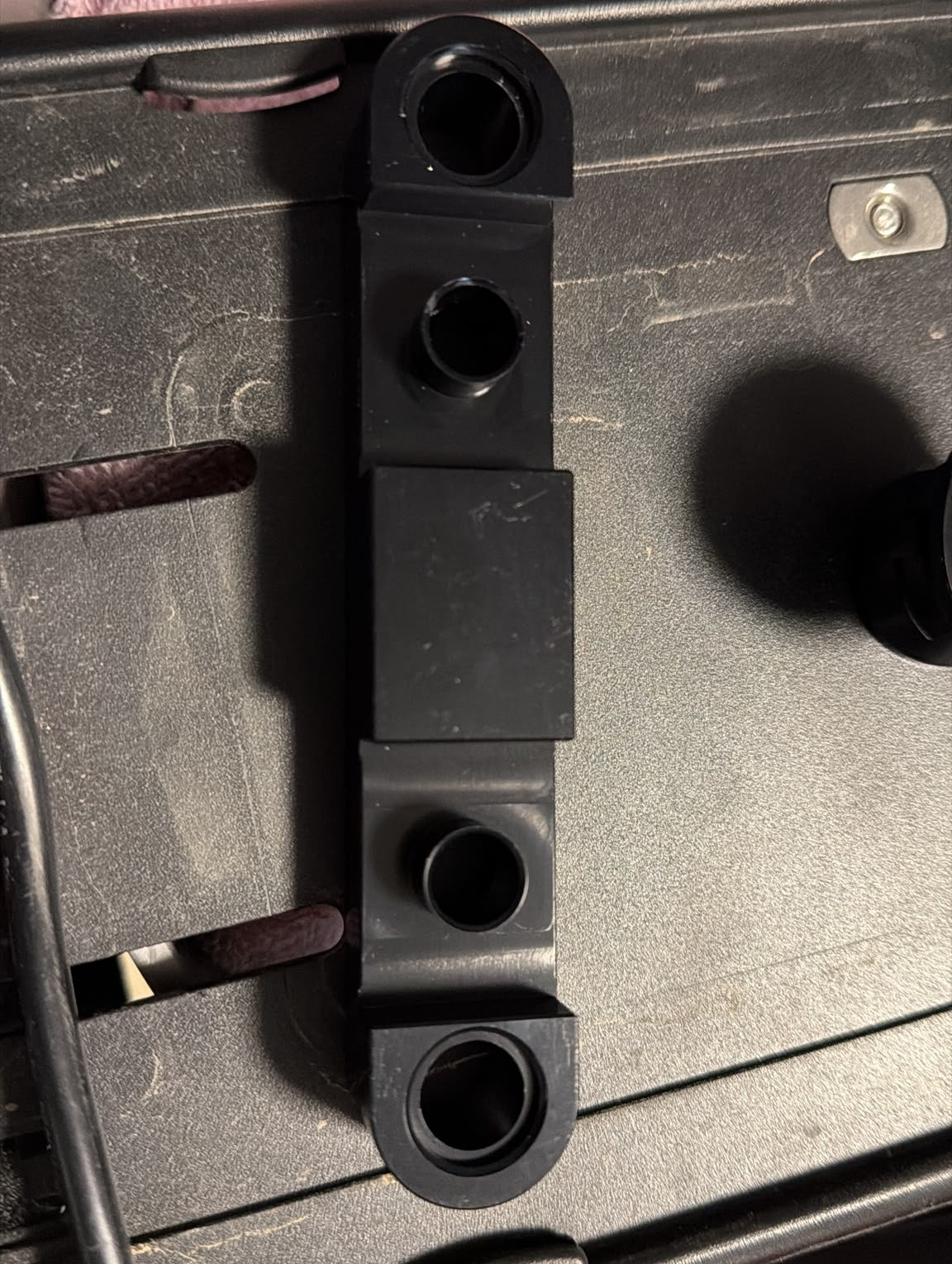 A close-up of a black steel bracket or hardware component attached to a dark surface
